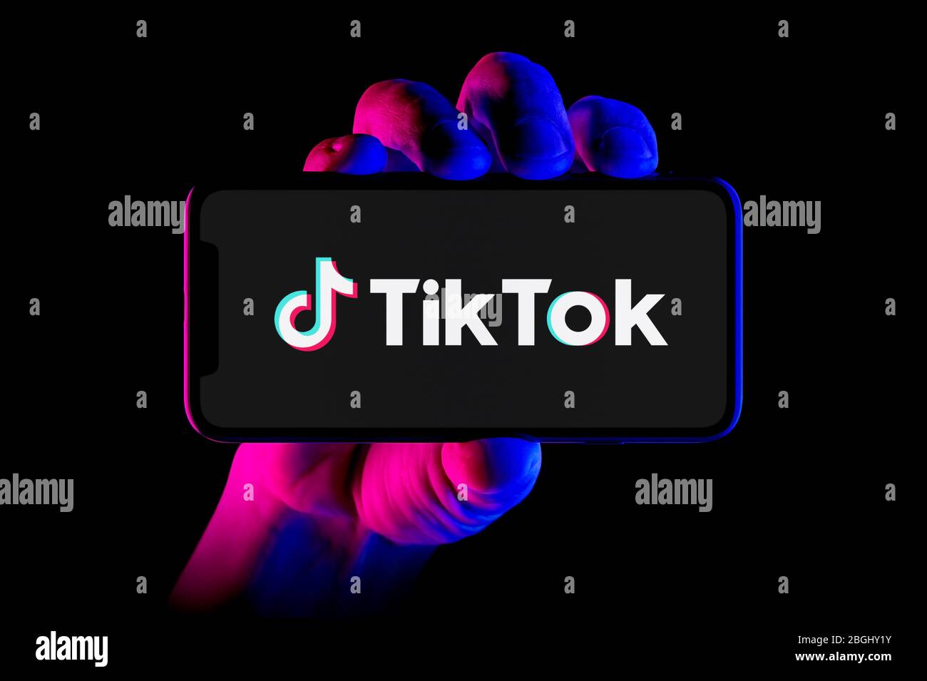 A smartphone displaying the Tik Tok logo is held by a hand shot on a black background (editorial use only). Stock Photo