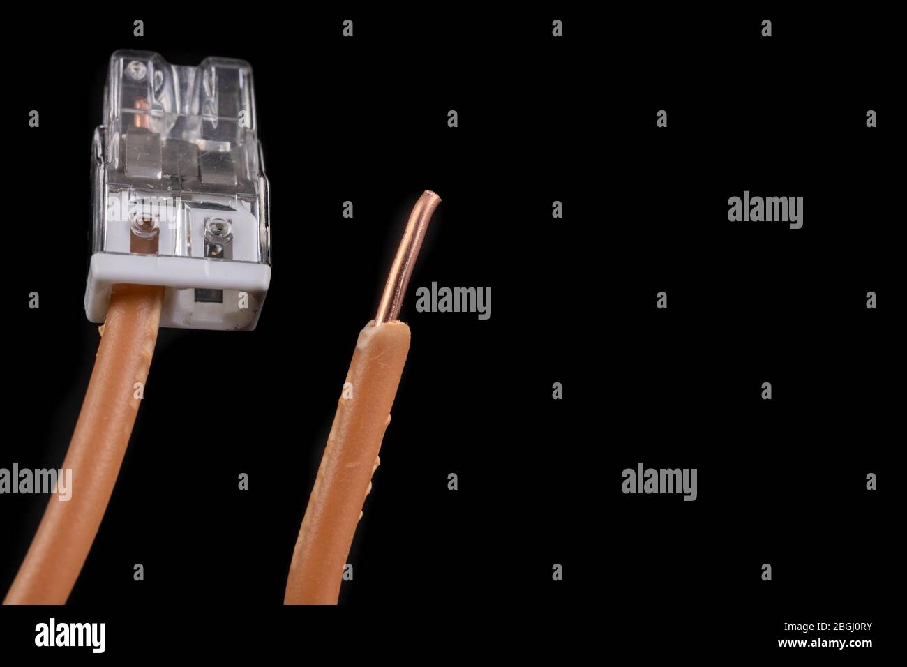 Two copper electric wires connected with a clamp. The method of connecting electrical installations. Dark background. Stock Photo