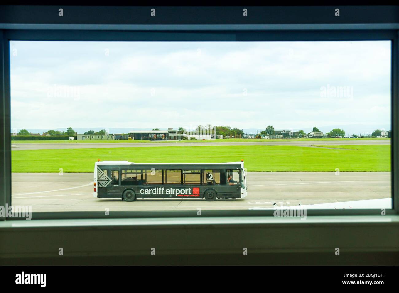 CARDIFF, WALES - JUNE 2019: Airport transfer bus driving across the apron at Cardiff Wales Airport.  The view is framed by a window in the terminal Stock Photo