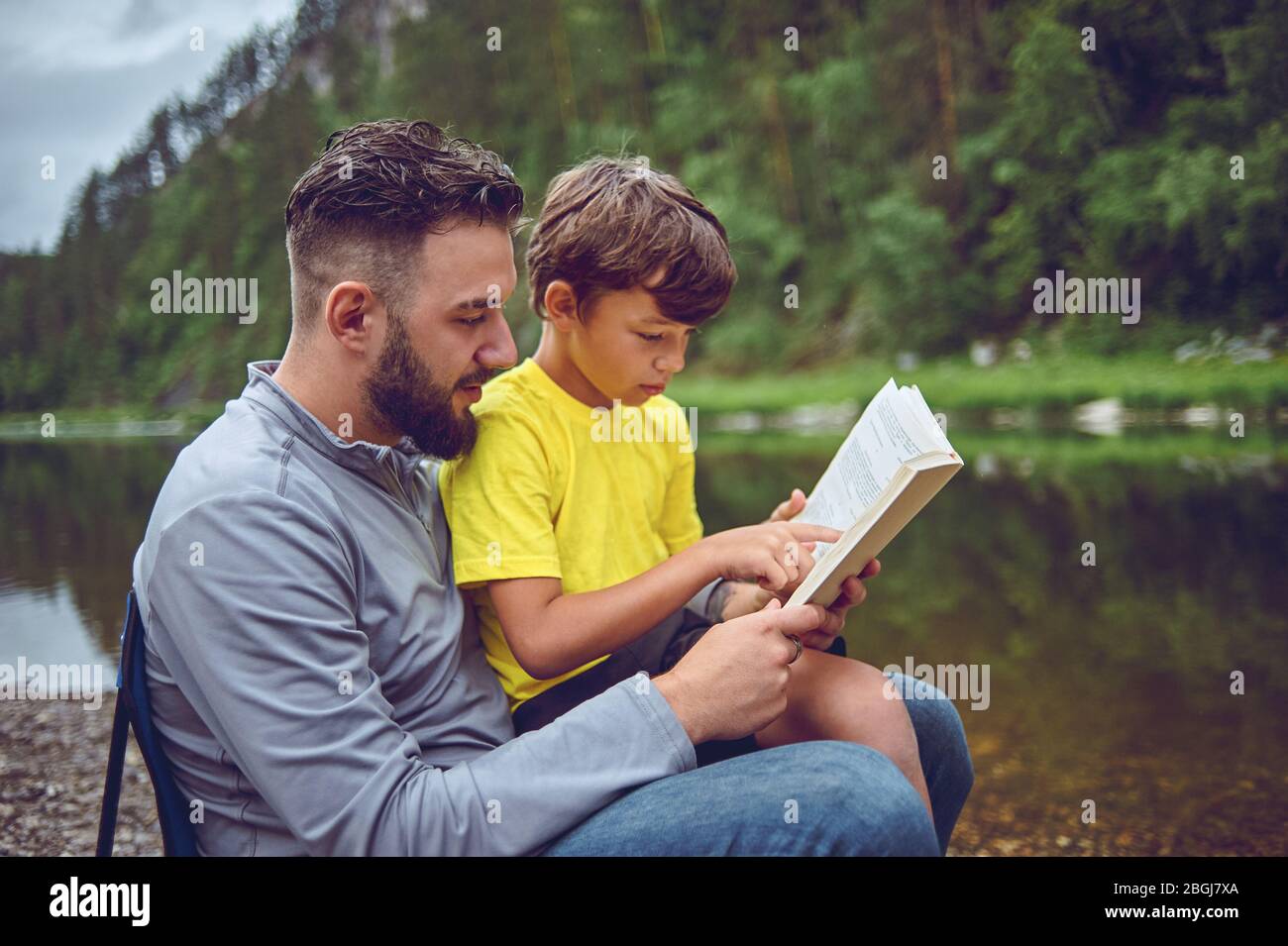 On a hike, on the river bank, father and son read a book Stock Photo