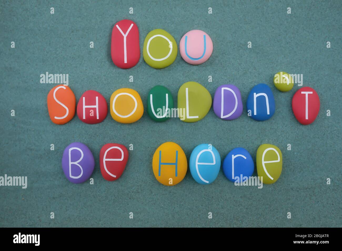 You shouldn't be here, negative phrase composed with multi colored stone letters over green sand Stock Photo