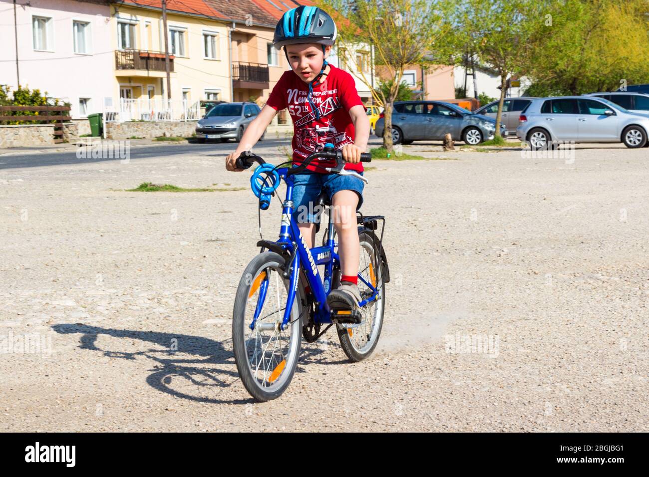 Boy child kid riding bike cycling while braking on dirt road in car park, Sopron, Hungary Stock Photo