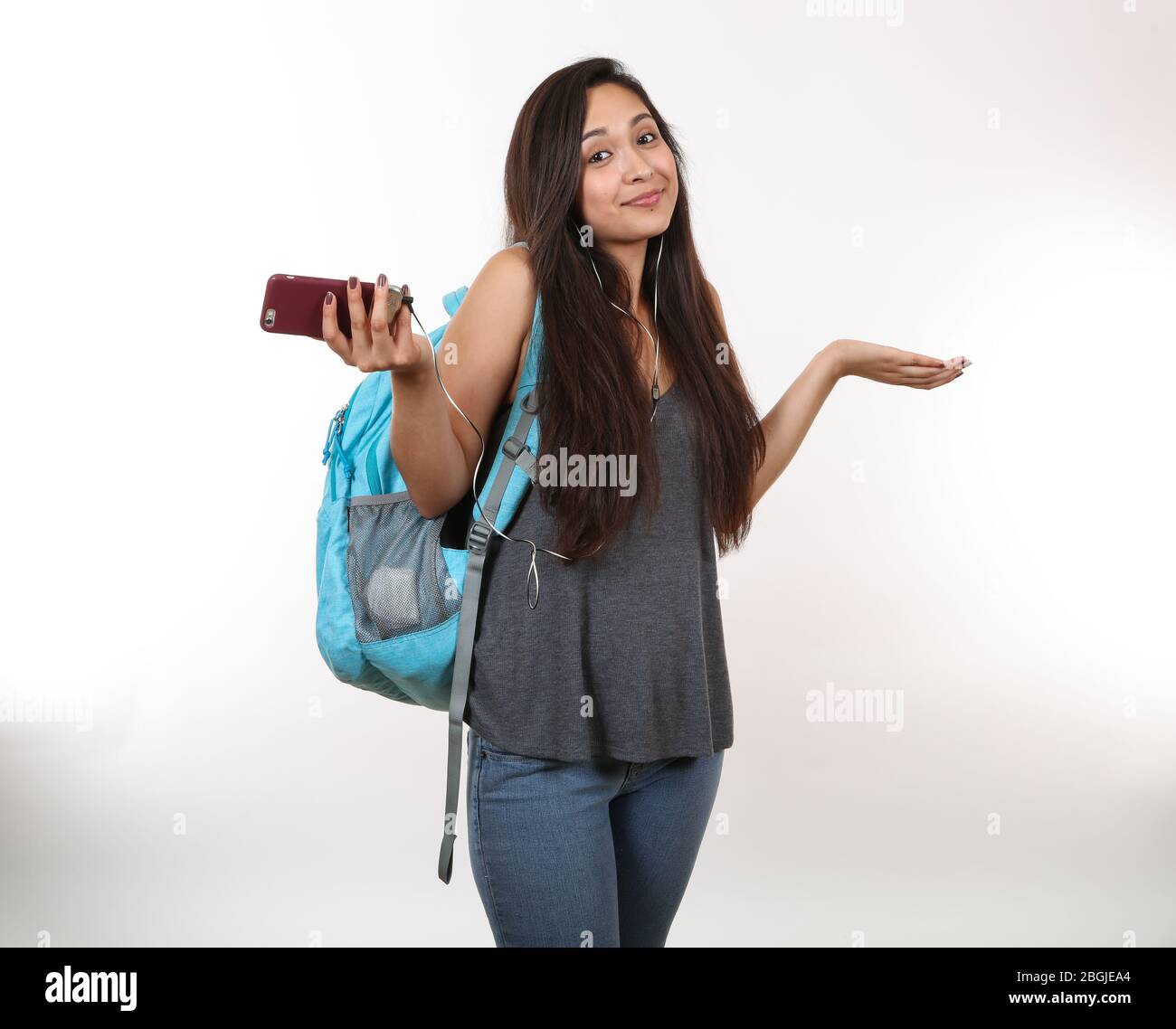 A young latina student wearing a blue backpack, holding her phone shrugs her shoulders.  Listening to music. Stock Photo