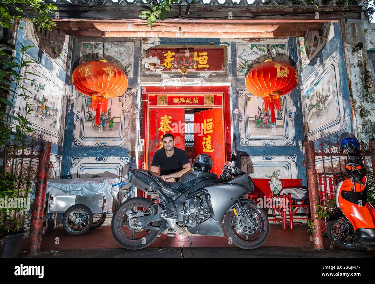 man leaning on his motorcycle in front of Chinese house in Bangkok Stock Photo