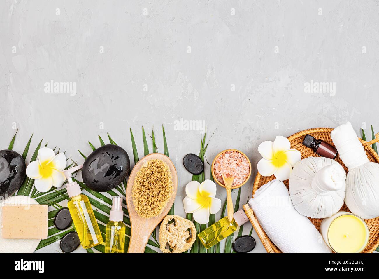 Spa massage Aromatherapy body care background. Spa herbal balls, cosmetics, towel and tropical leaves on gray concrete table. Top view, flat lay Stock Photo