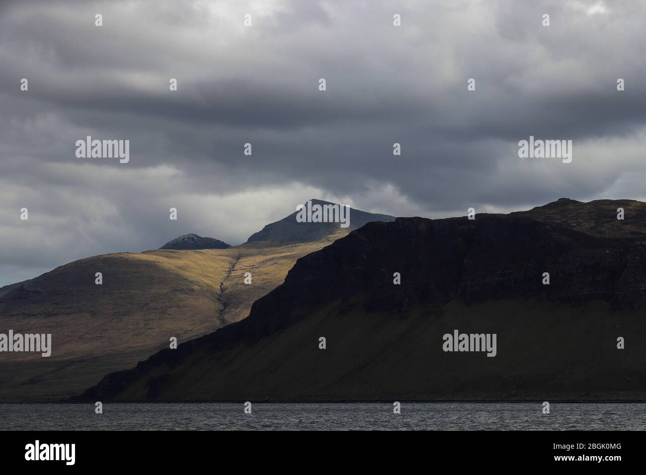 View of Ben More, Isle of Mull, Scotland from Loch Na Keal on a blustery  day, clouds overhead. Patch of sunlight behind dark Dunan Na Nighean cliffs. Stock Photo