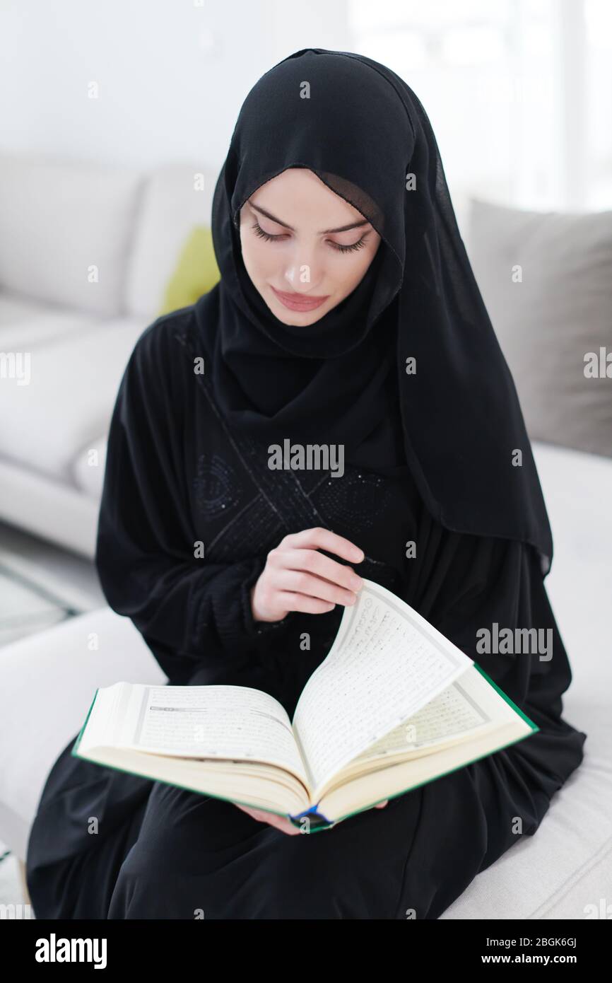 young traditional muslim woman reading Quran on the sofa before iftar dinner during a ramadan feast at home Stock Photo