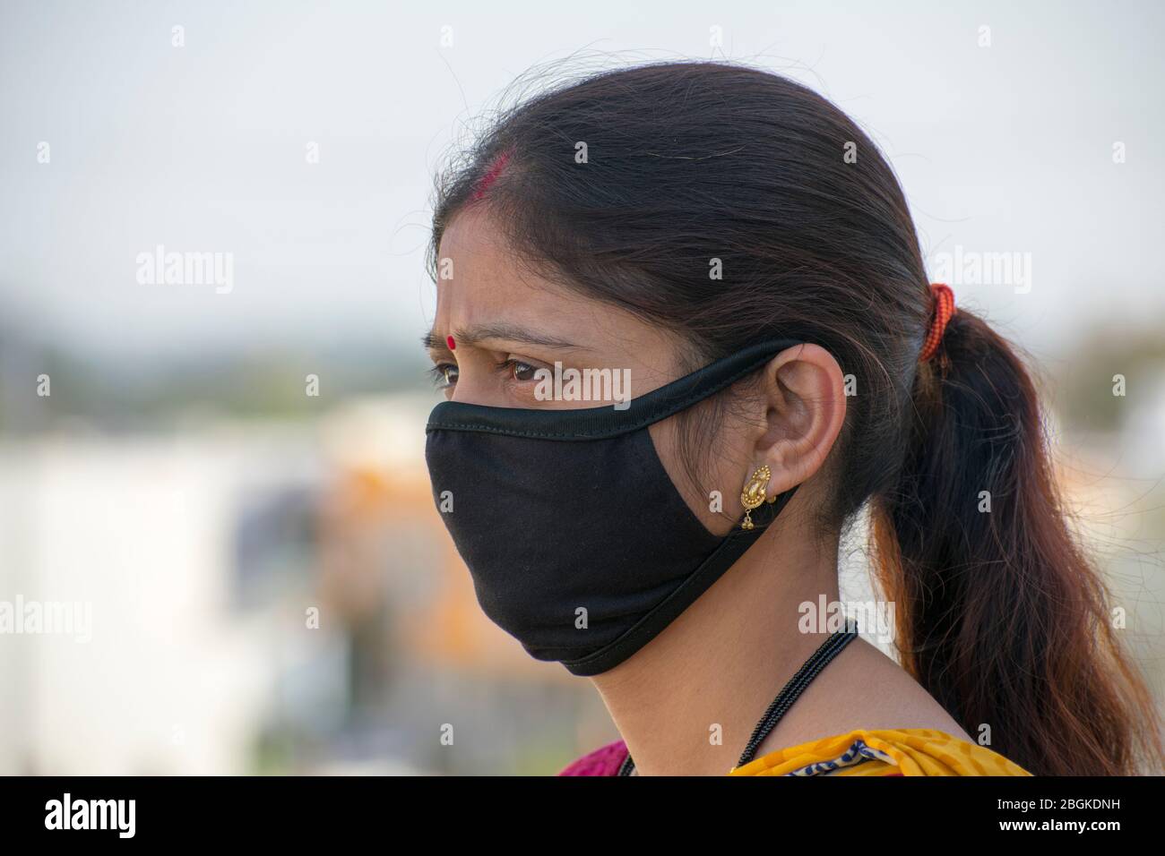 Detail of Indian woman wearing a Black face mask.Side view face, blurred background. Corona virus, COVID-19 quarantine. Mask as protection. Stock Photo