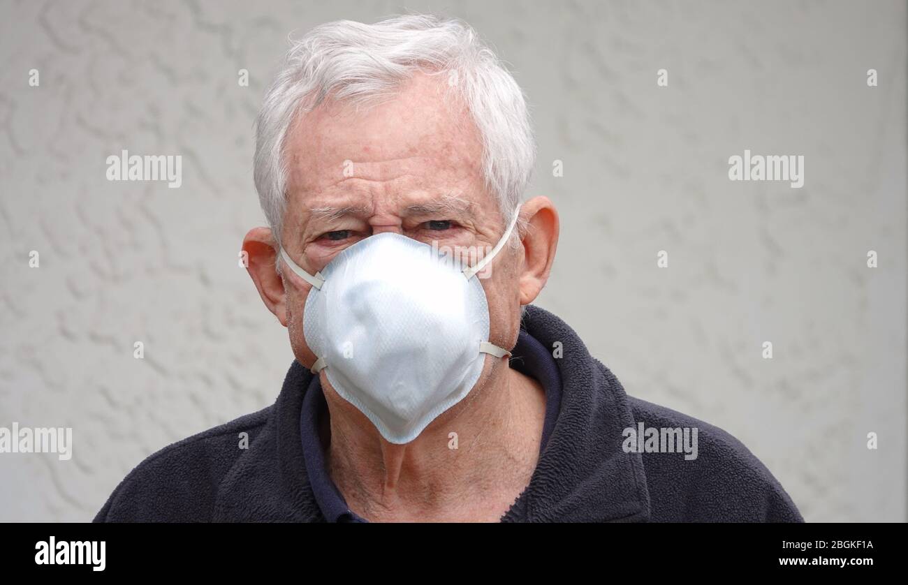 Distressed looking senior (80 year old Caucasian man) wearing a face mask to protect himself from Coronavirus Stock Photo