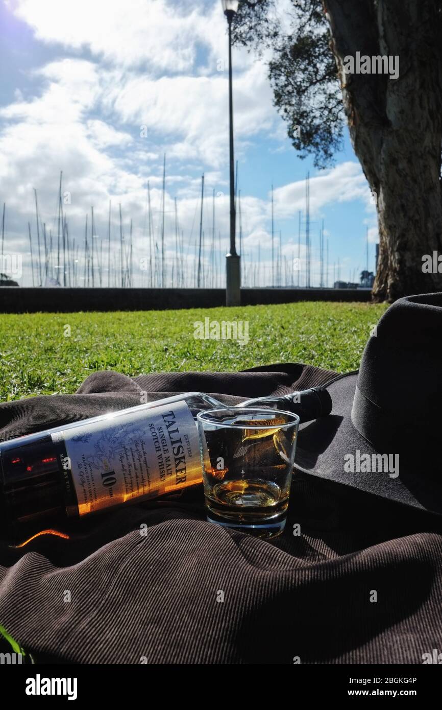 Talisker 10 year single malt scotch whisky photographed in Rushcutters Bay park Sydney, green grass, a fedora hat, cord jacket, a glass of whisky Stock Photo