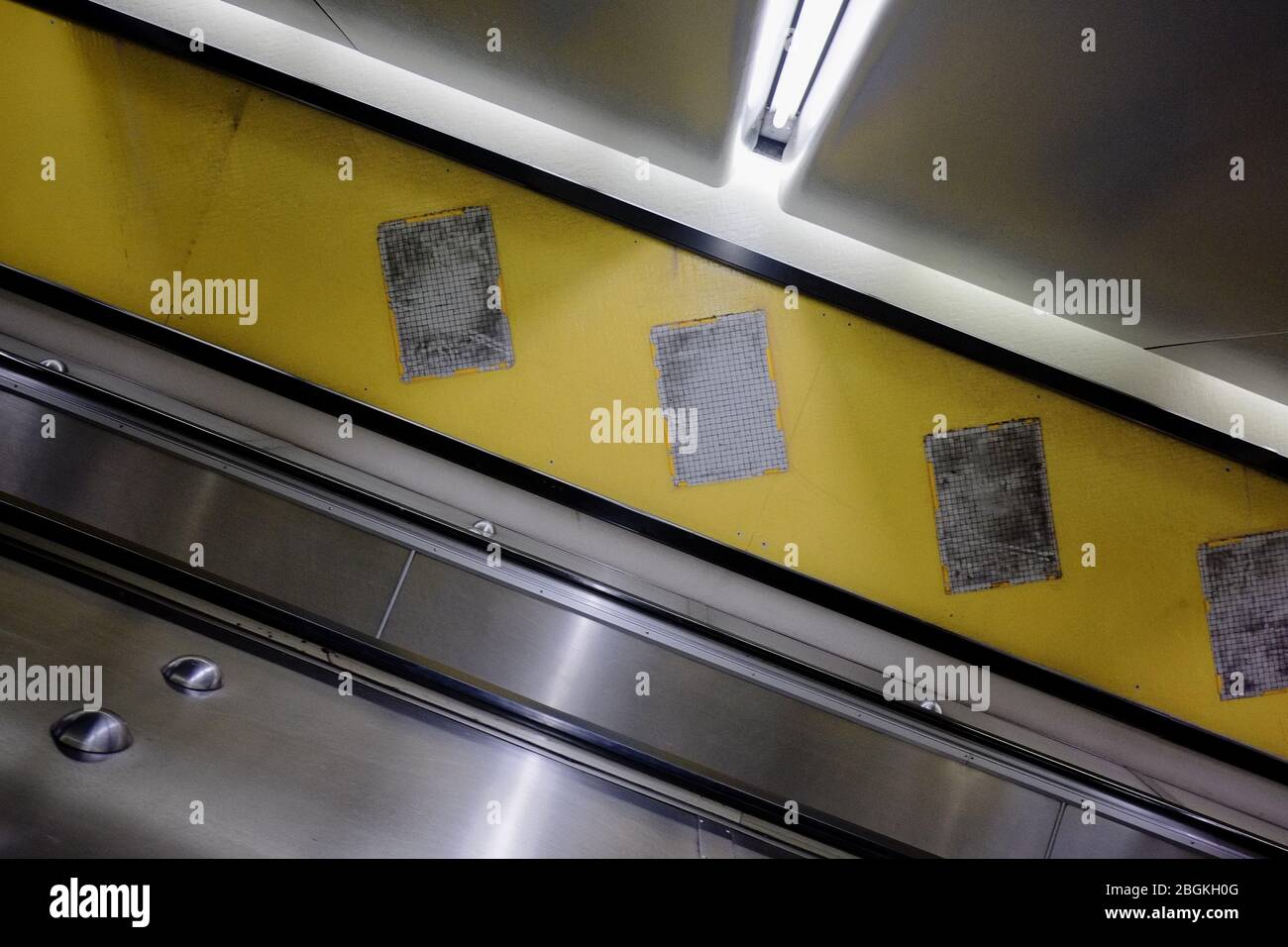 Escalator at an acute angle with exposed tile walls, a blank space where posters have been removed from a yellow painted at Kings Cross Station Sydney Stock Photo