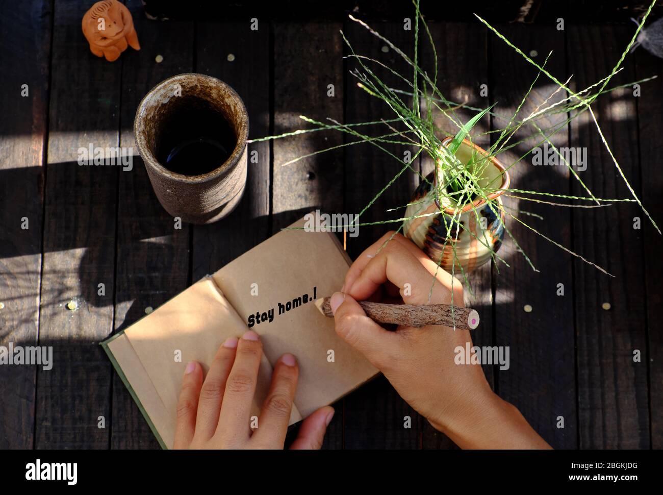 outdoor table, woman hand hold a piece of paper with STAY HOME message in epidemic season by corona virus, notebook, pencil ready for work at home Stock Photo