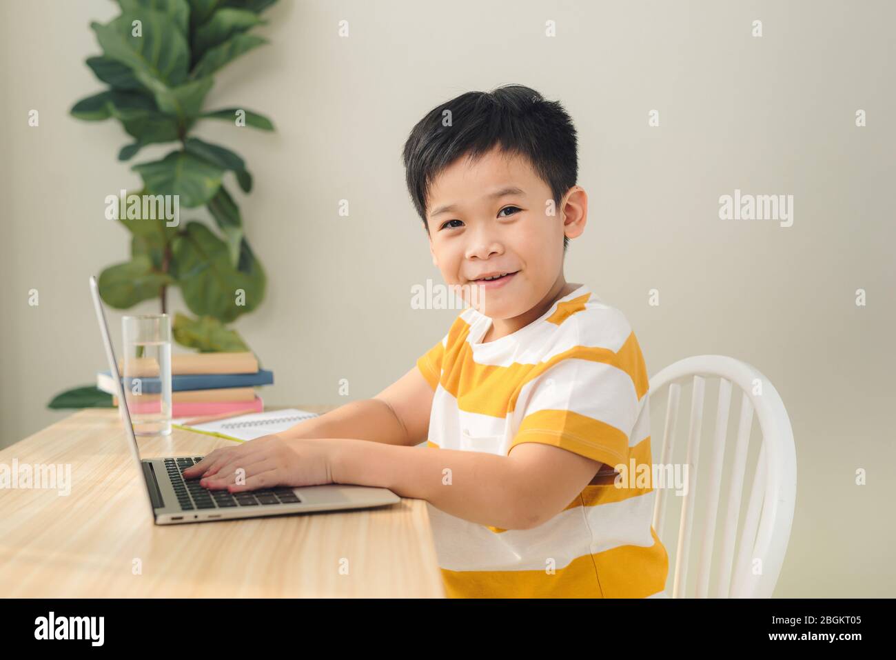 Smart looking Asian preteen boy writing and using computer laptop studying online lessons. Stock Photo