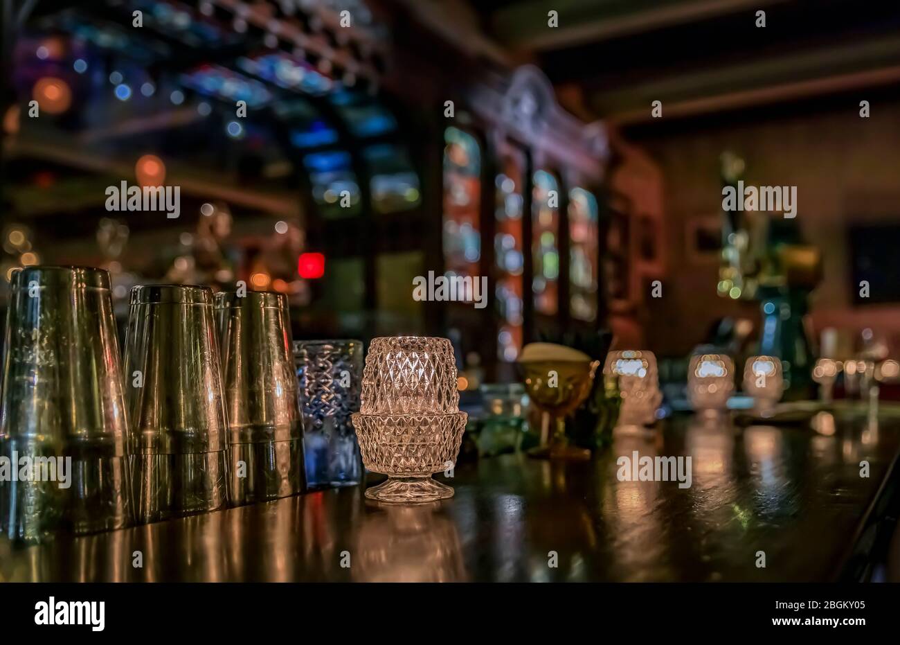Vintage wooden bar counter with candles in glass holders, bar tools and a blurred view of a baroque or Victorian bar with bottles in the background Stock Photo