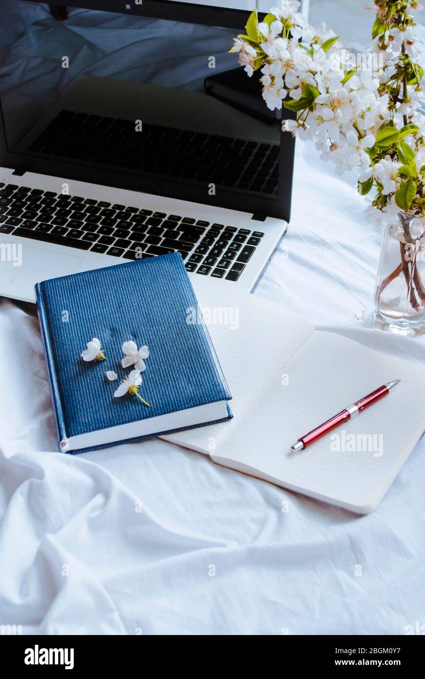 Open laptop on the bed, spring flowers, notepad. Work at home. Home