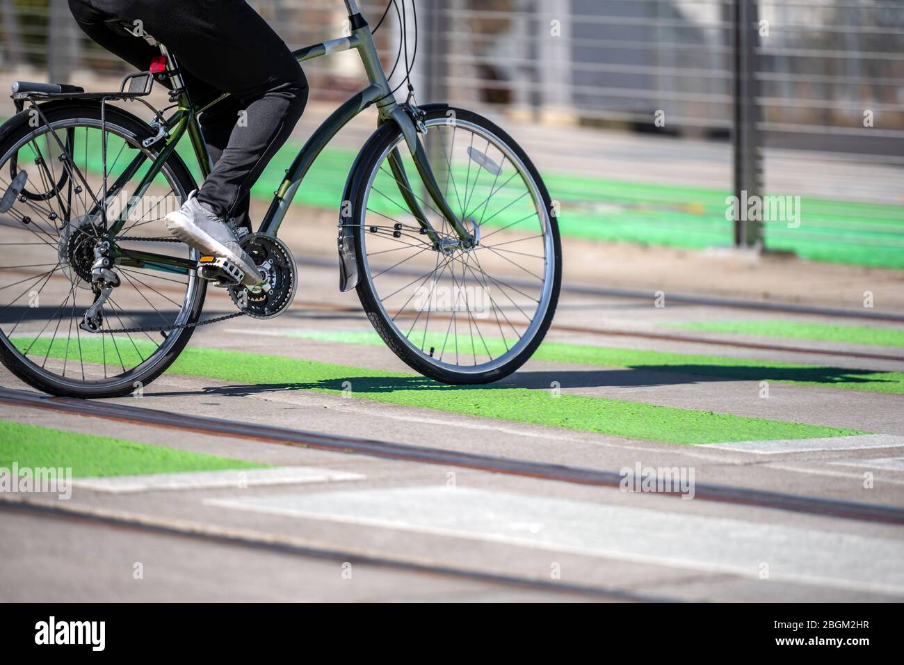 A man on a bike pedals a bicycle crosses tram tracks on a dedicated crossing for cyclists and pedestrians preferring healthy lifestyle using cycling r Stock Photo