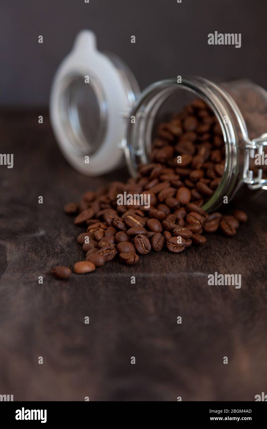 Jar with coffee beans rashes on a wooden table. Coffee background close ...