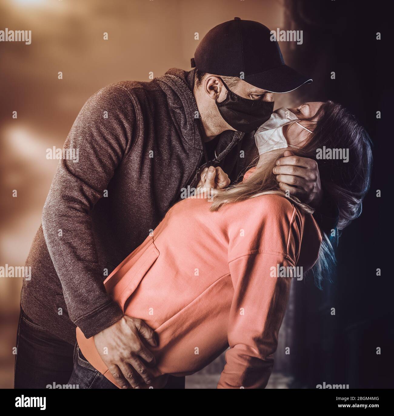 A young adult man kisses a woman in protective medical masks on a city street at night. Coronavirus victory concept and love Stock Photo