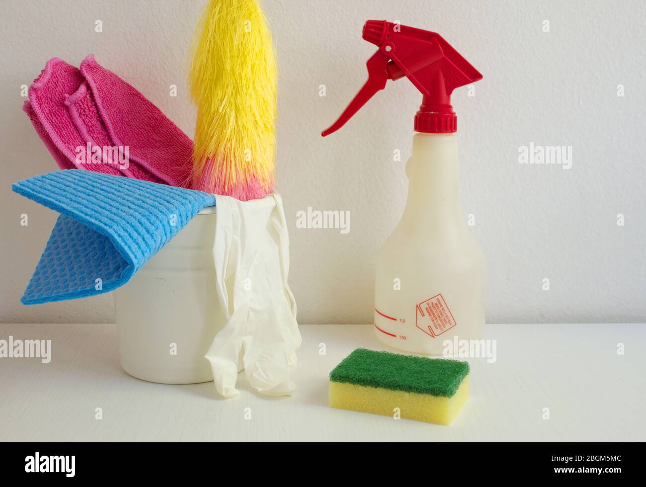 Container with cleaning items on the white table against white wall Stock Photo