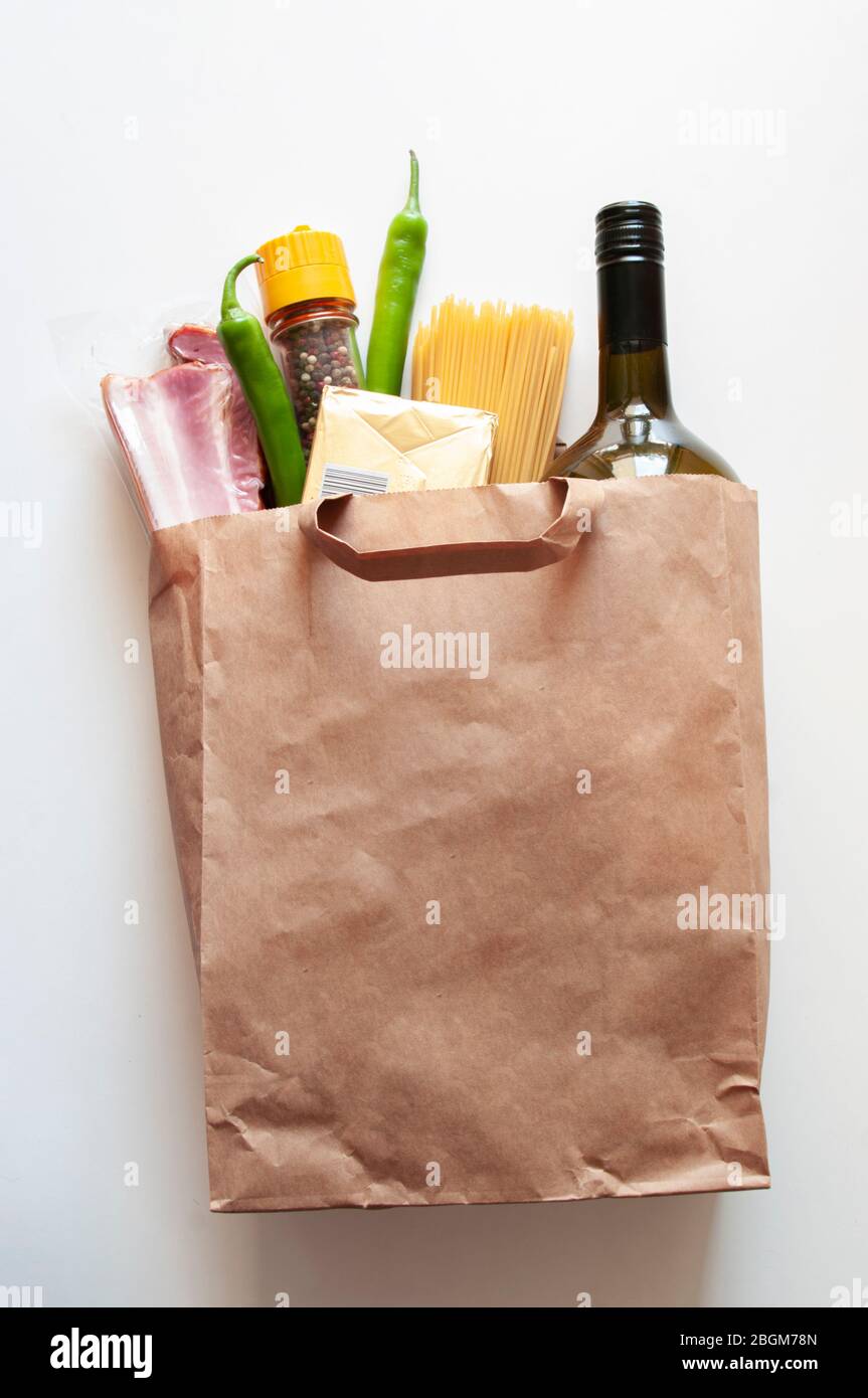 Paper bag with Food supplies, crisis food stock for quarantine isolation period,. salad, pasta, butter,wine,chilli, bacon. Food delivery, donation Stock Photo