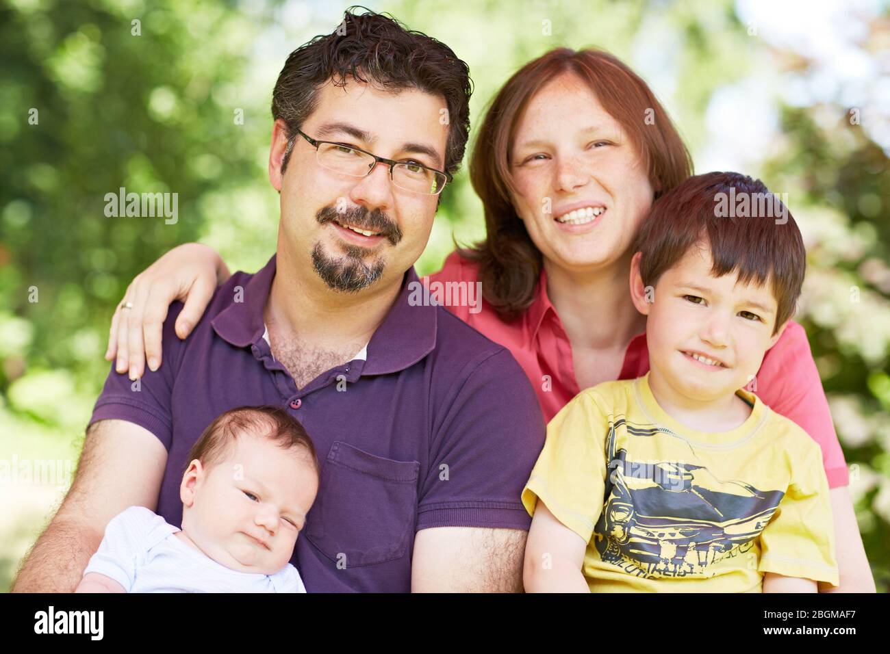 Glückliches Portrait mit Vater, Mutter, Kind und Baby im Grünen Stock Photo