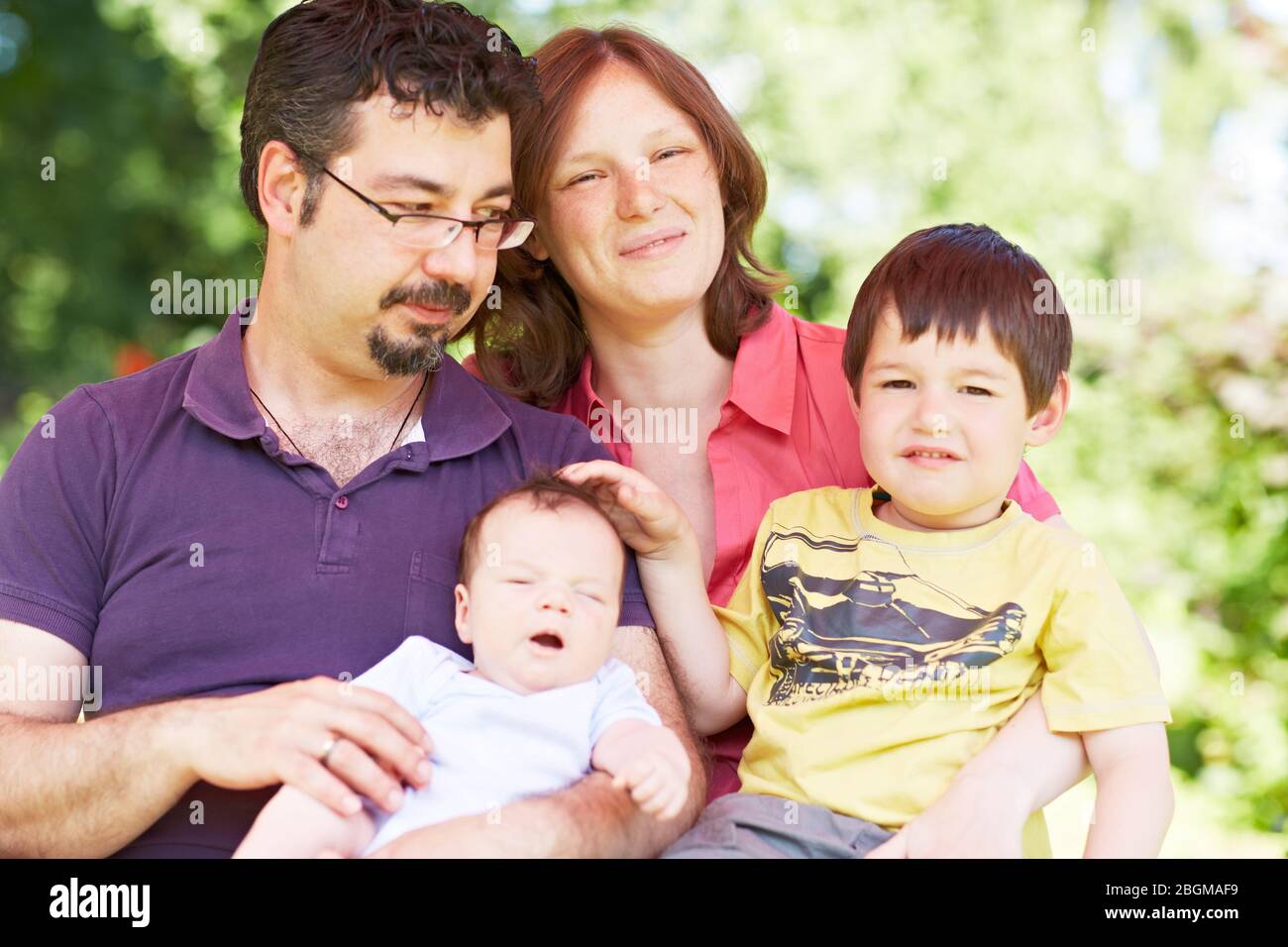 Glückliche Familie mit Kind und Baby sitzt im Grünen Stock Photo