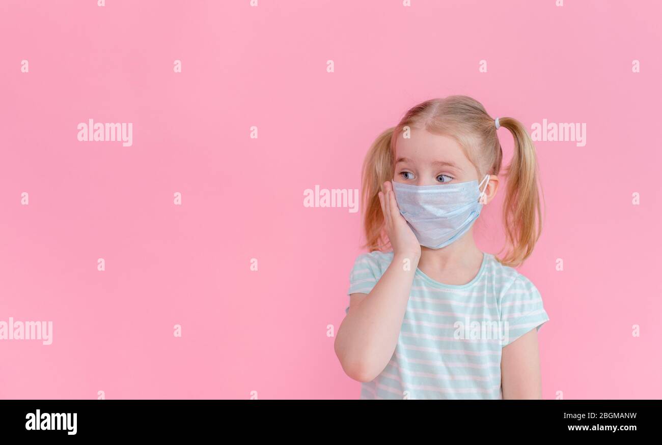 Little blonde girl with two ponytales in a medical mask face on a pink ...