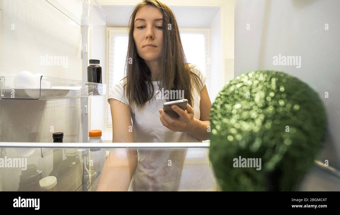 woman at fridge with smartphone making list of necessary food at home kitchen. Smart shopping
