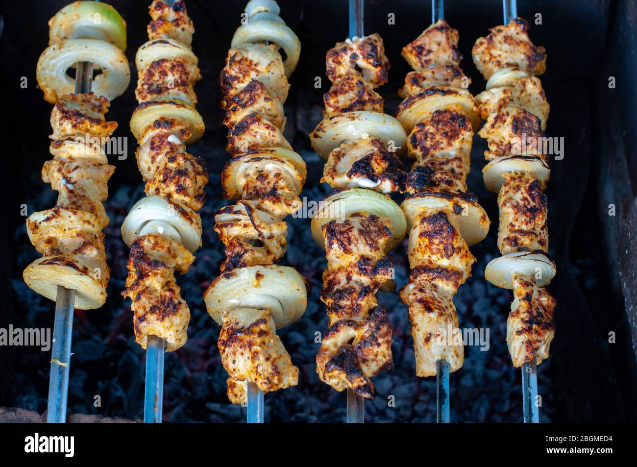 Top view of homemade chicken shish kabobs with fresh onions. Grilled chicken meat skewers on dark background. Delicious food for picnic. Stock Photo