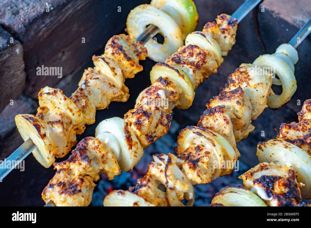 Roasted meat shashlik closeup. Homemade chicken shish kabobs with fresh onions. Grilled chicken meat skewers on dark background. Delicious food for pi Stock Photo