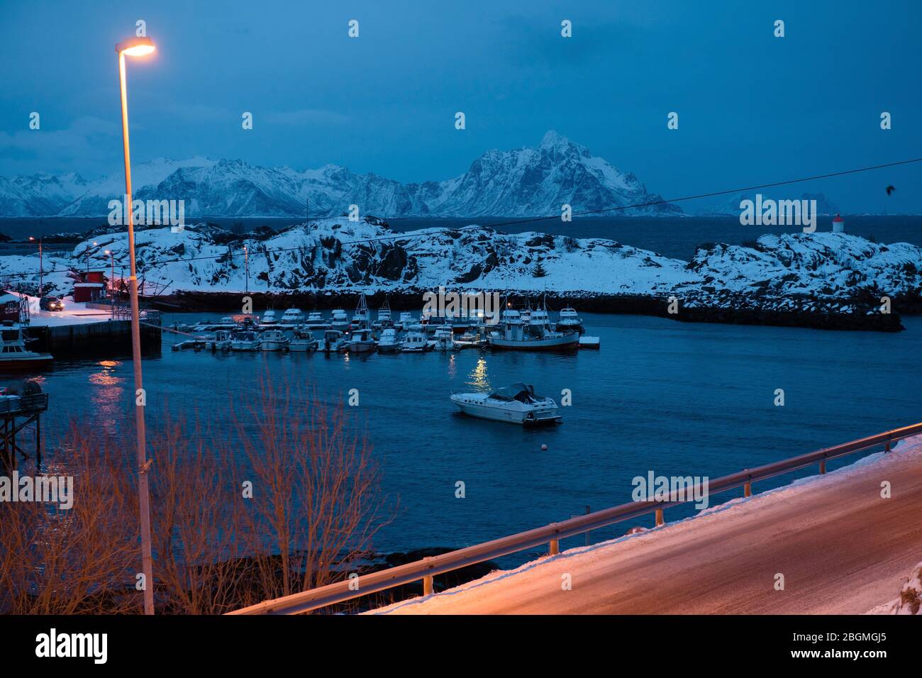 Fishing village, city lights, snowy mountains, sea, blue cloudy sky reflected in water at night in winter. Landscape at night in Lofoten islands Stock Photo