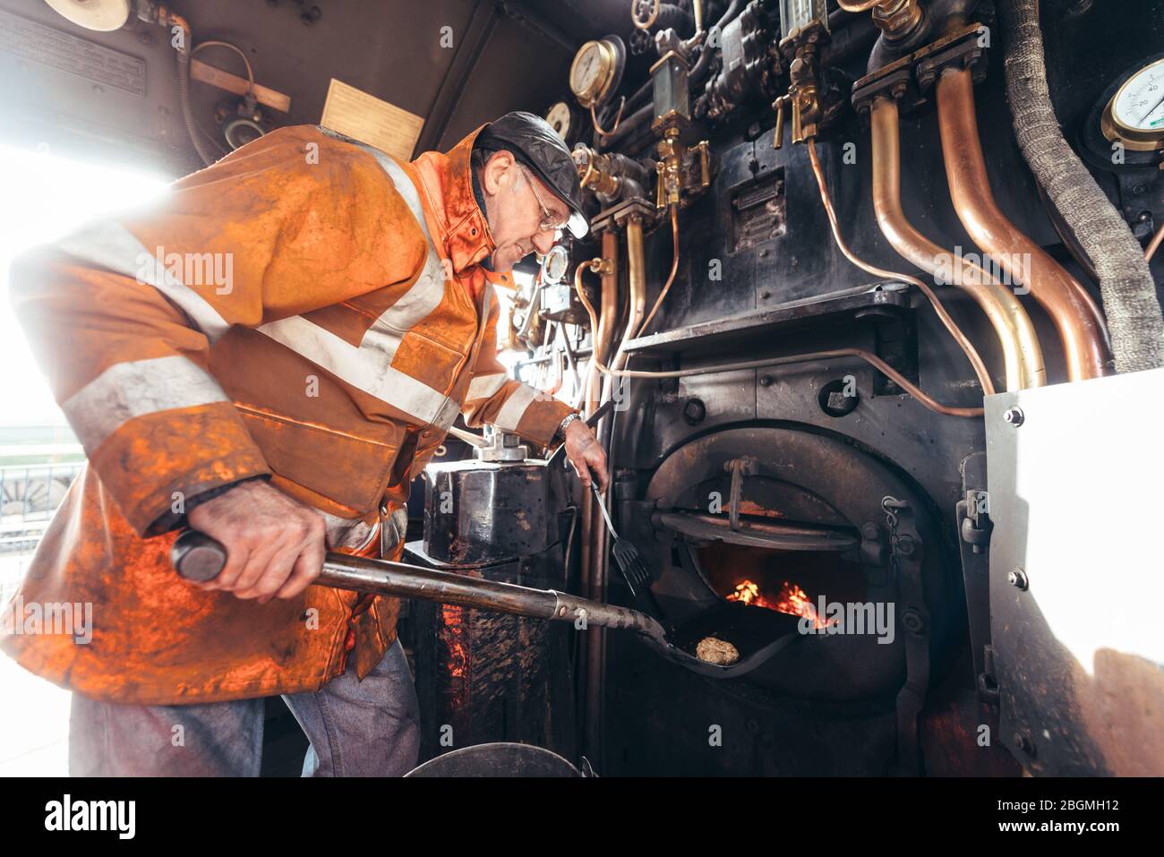 A man holding a spatula using an oiled shovel to cook food in the firebox   Working British steam locomotive, the Sir Nigel Gresley (LNER Class A4 Pac Stock Photo