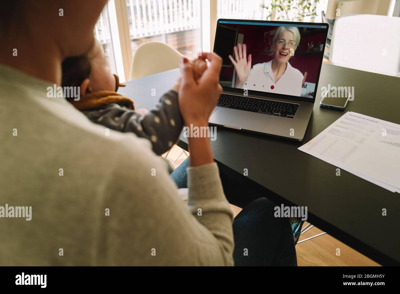 Woman with her daughter having video call with her mother. Woman connecting with her mother on a video call while at home. Stock Photo