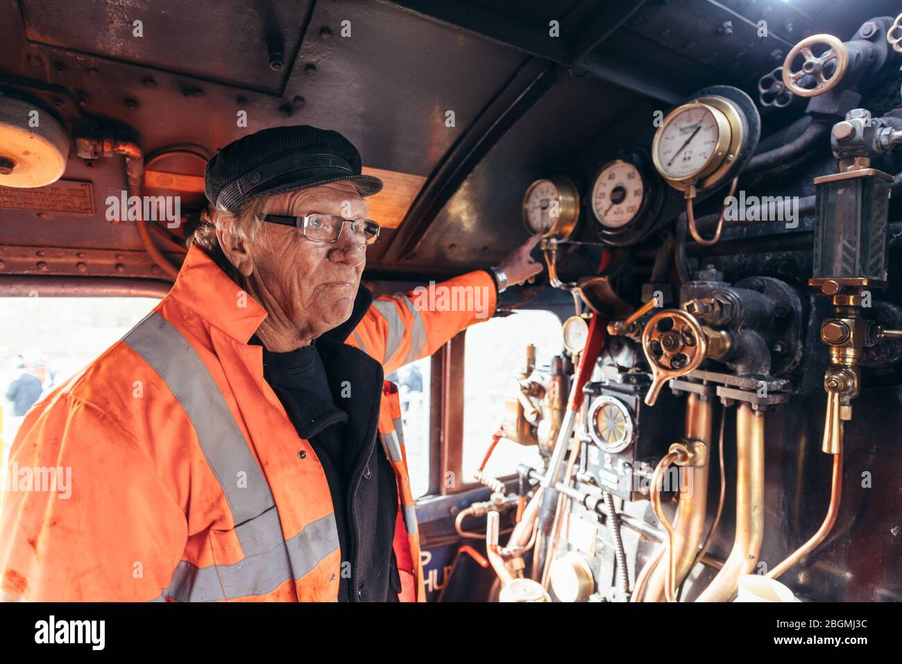 A man takes a break whilst leaning inside the cab, with brass dials and copper pipes in the background   Working British steam locomotive, the Sir Nig Stock Photo