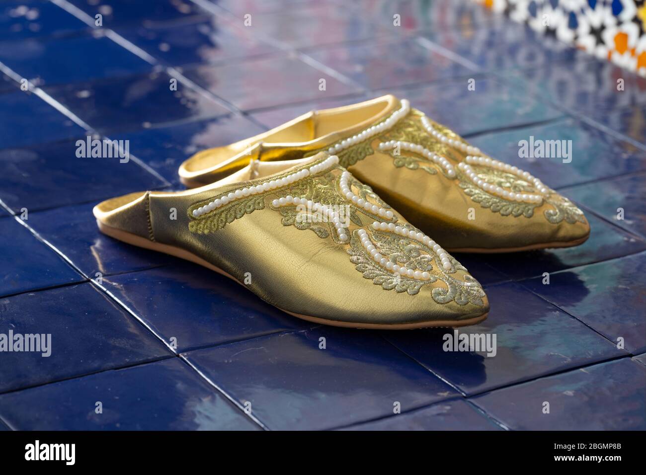Traditional Moroccan pair of festive golden slippers at a floor with blue tiles Stock Photo