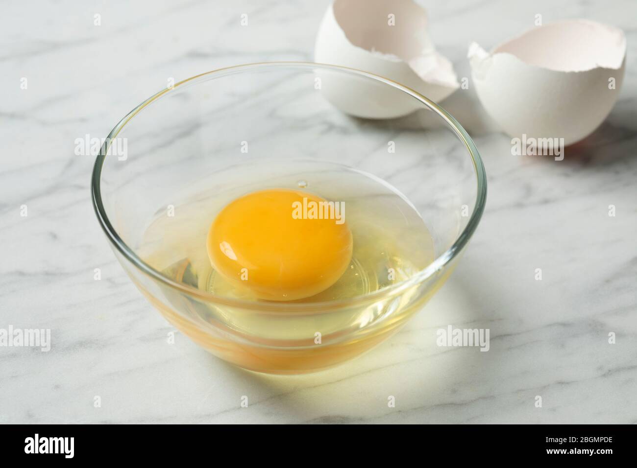 Fresh raw egg in a bowl close up with white shells in the background Stock Photo