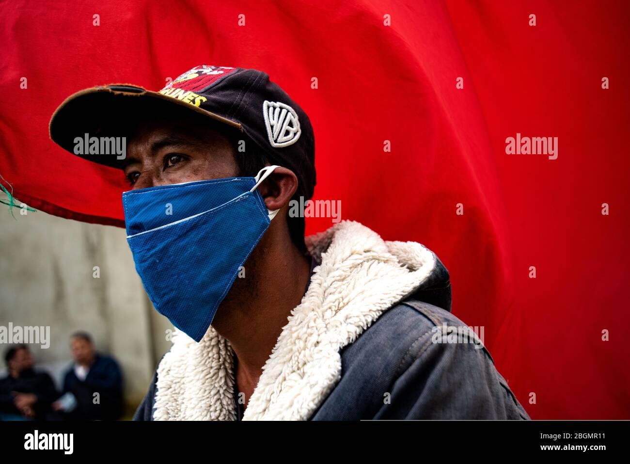 Ciudad Bolivar, Colombia. 21st Apr, 2020. A man with a mouthguard stands in  front of a red flag in the Ciudad Bolivar district south of Bogota. Red  scarves have become a symbol