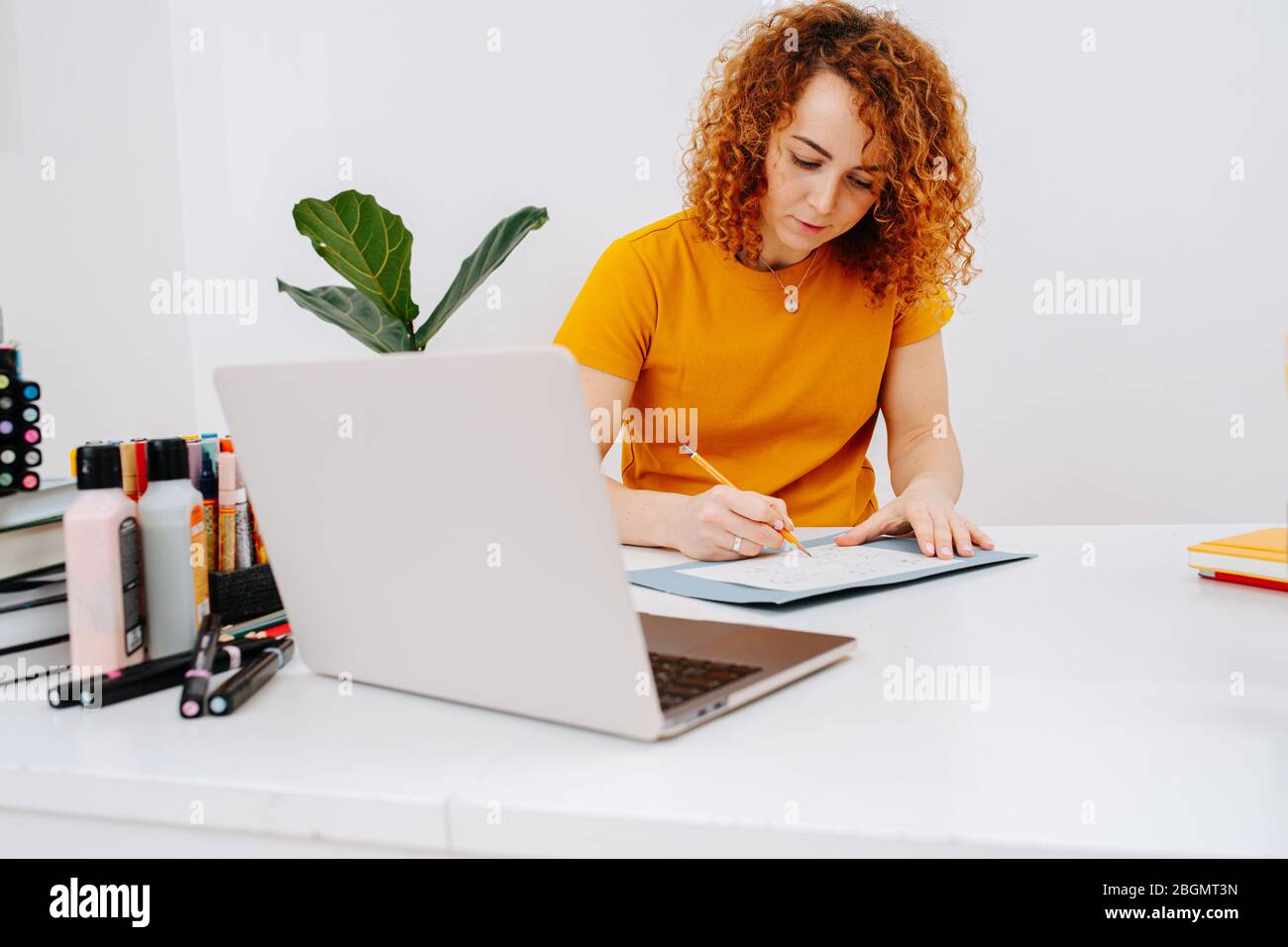 Serious artist woman drawing behind work desk, rushing it to catch up Stock Photo