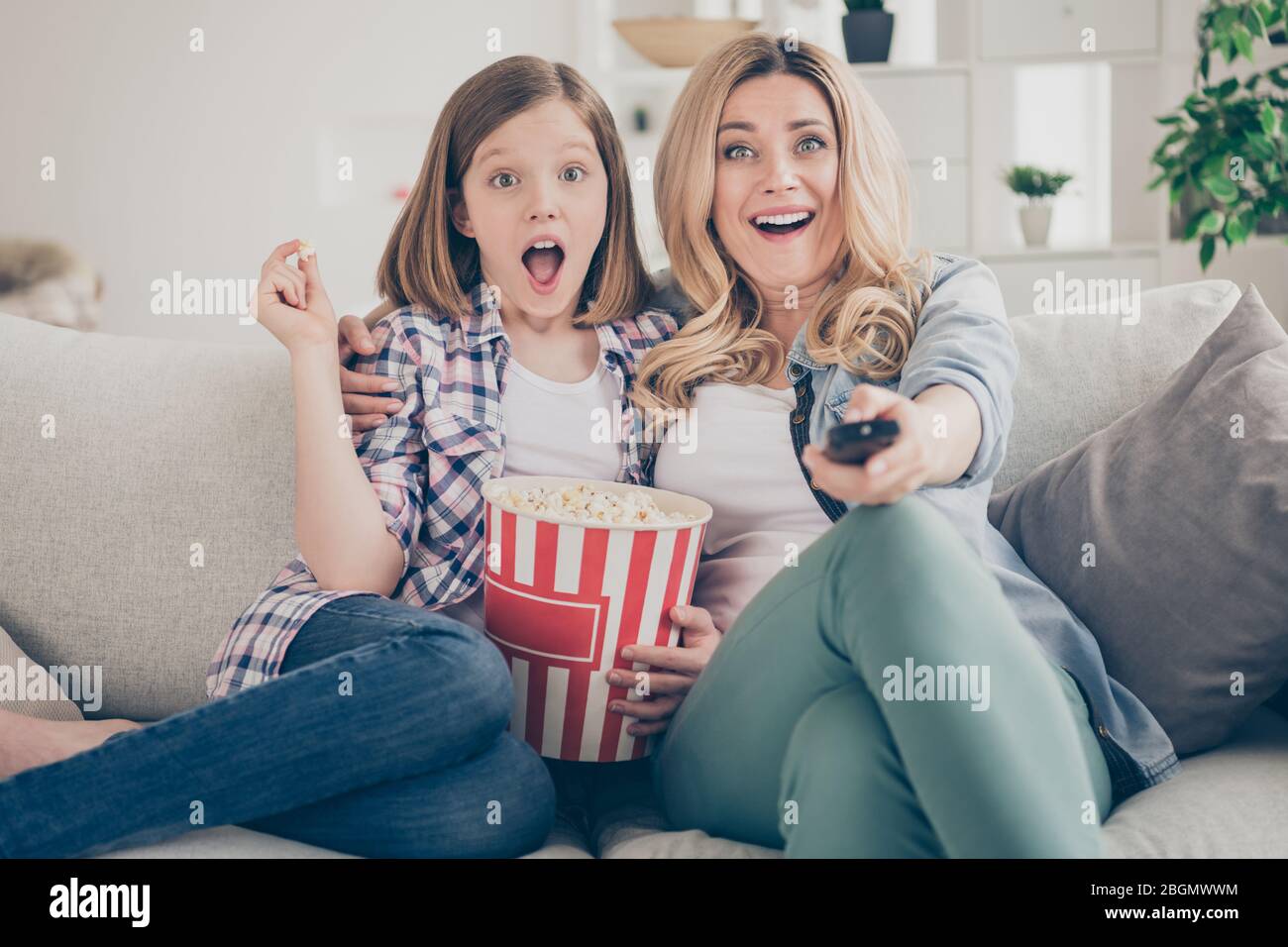 Photo of funny shocked lady mom daughter sit sofa hugging eat popcorn