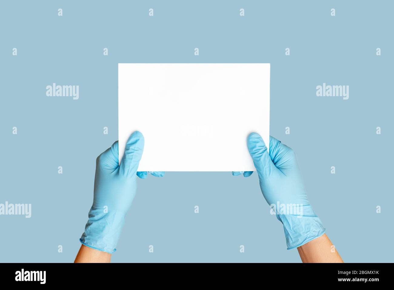 Hands in medical gloves holding empty blank on blue background. Stock Photo