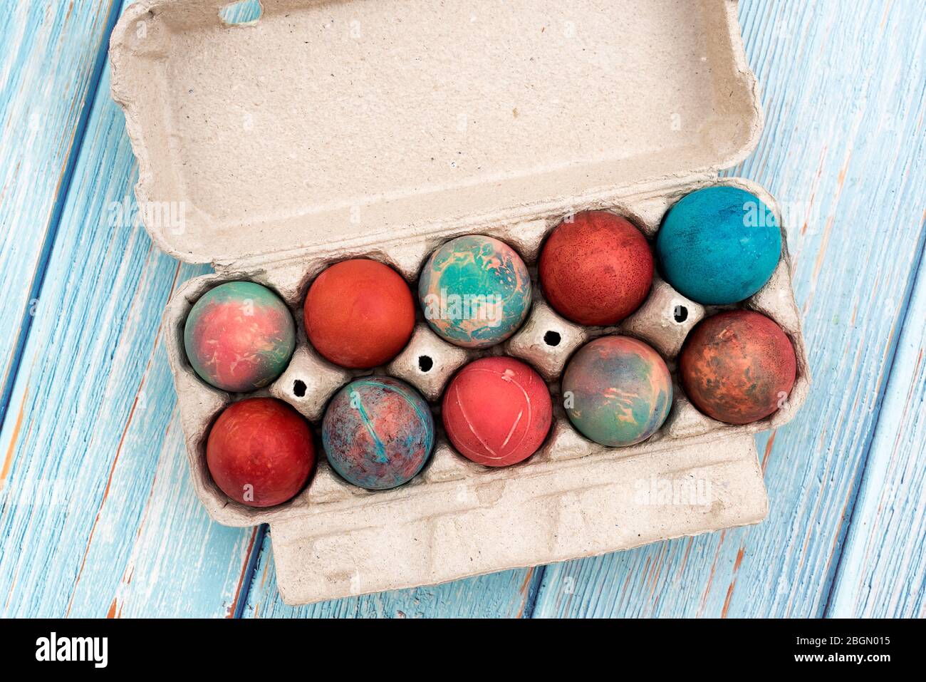 Colorful Easter eggs in cardboard egg box on white background. Raw chicken eggs in open egg box on a blue wooden table. Eggs in the package. Top View Stock Photo