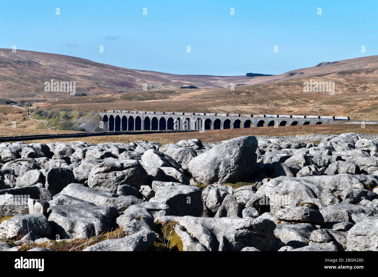 The train carrying stone from Arcow Quarry crosses Ribblehead Viaduct, Yorkshire Dales National Park, UK. Limestone pavement in the foreground. Stock Photo