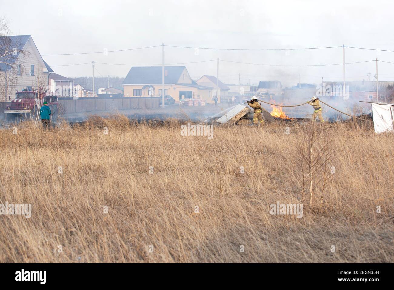 firefighters in fire fighting equipment battle fire dry grass in spring. Azov German national district of Omsk region, Russia, 18.04.2020. Stock Photo
