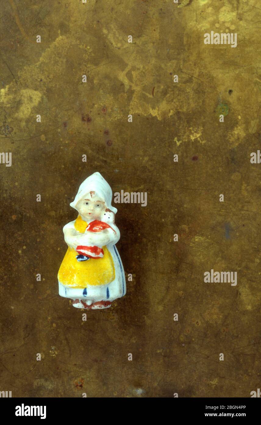 Small china model of girl in national Dutch dress holding doll with tarnished brass background Stock Photo