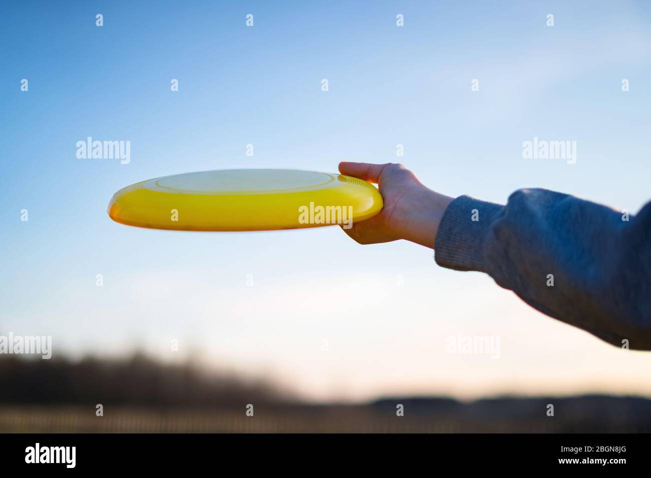 Hand holding yellow frisbee outside. Flaying frisbee outdoors with blue