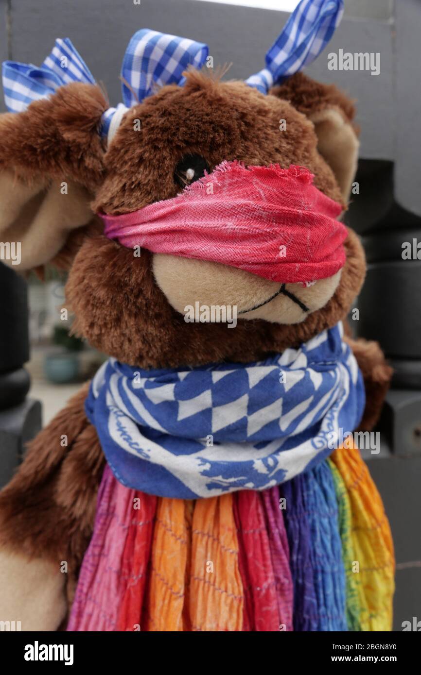Cute brown teddy bear wearing a rainbow colored dress and blue and white  ribbon on head with red scarf face mask attached to front gate for kids  Stock Photo - Alamy