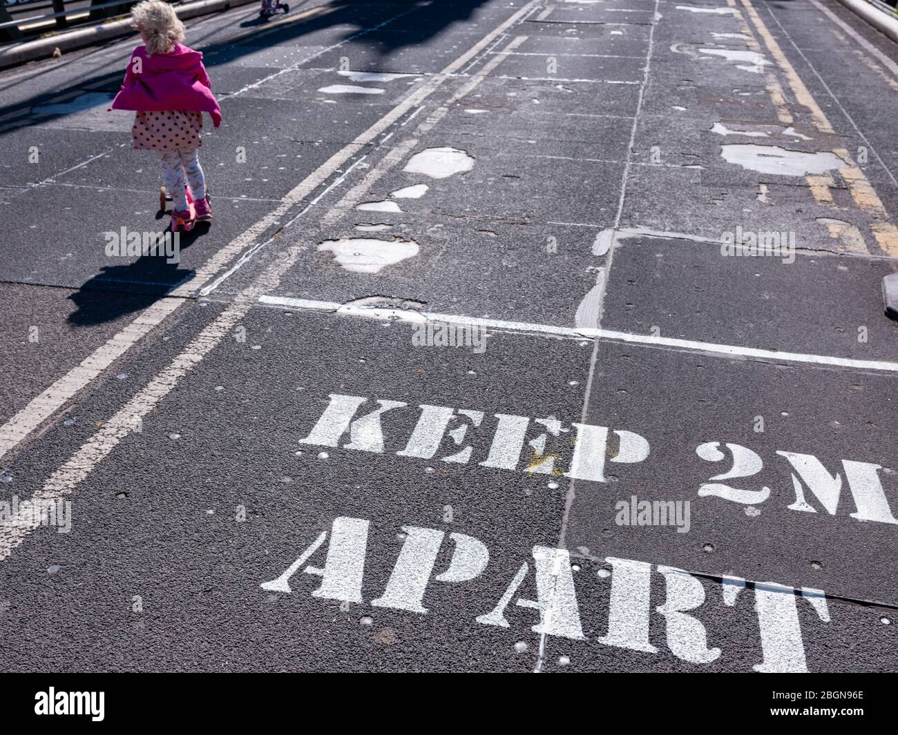 5th April 2020 A sign painted on the road surface warns pedestrians to keep their distance in order to prevent the Covid-19 virus spreading. A two yea Stock Photo