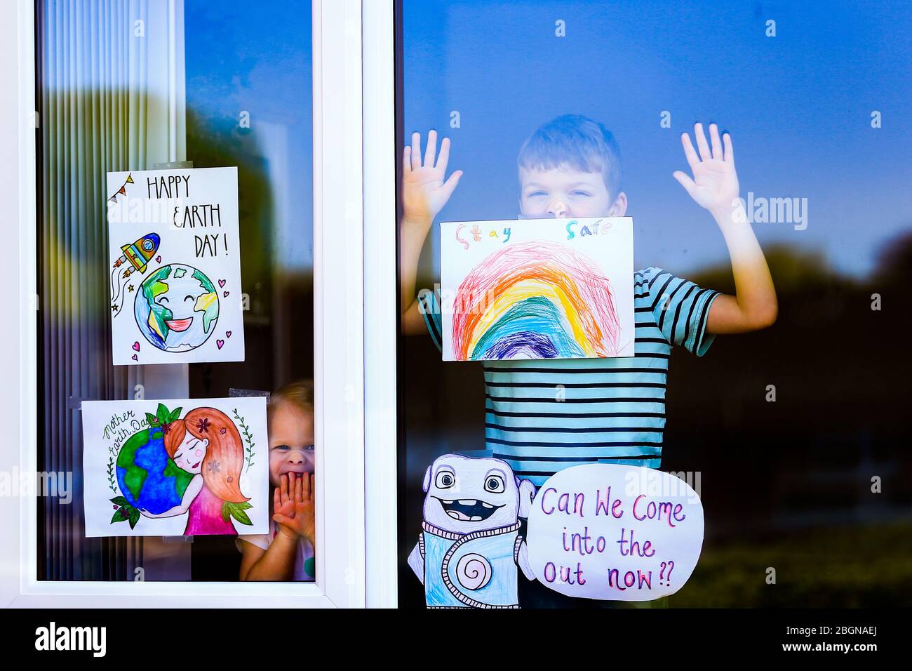 Droitwich, Worcestershire, UK. 22nd Apr, 2020. 7-year-old Will Keight appears at the window of his home in Droitwich Spa with his young sister Orla, 2, with the posters they have made for World Earth Day and the NHS. [Note: parental permission granted] Credit: Peter Lopeman/Alamy Live News Stock Photo