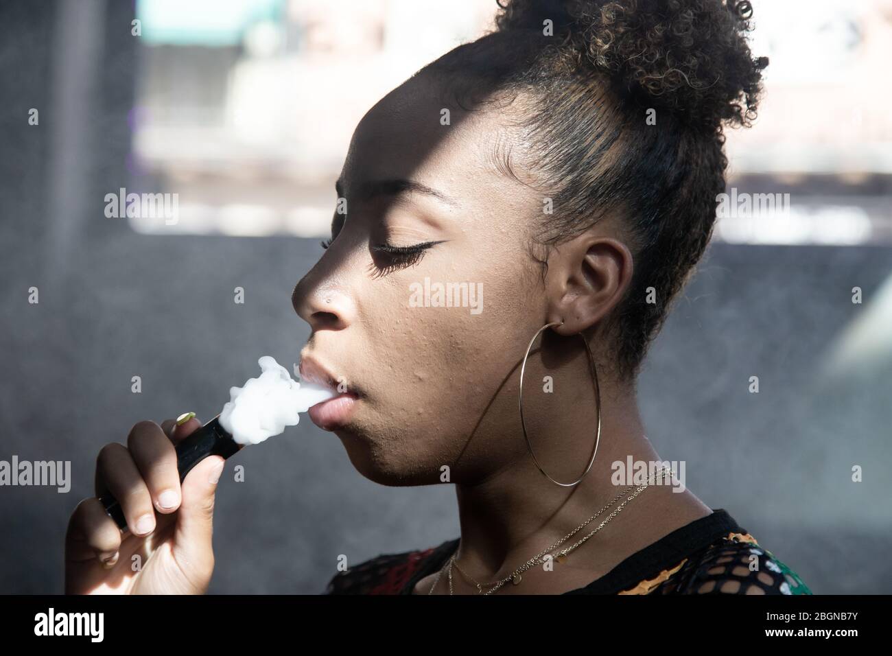 Profile of a black girl with big rings smoking with a steamer and blowing  smoke with her eyes closed inside a room Stock Photo - Alamy