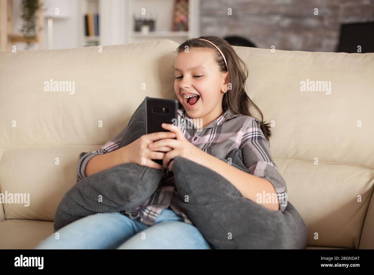 Happy little girl sitting on the couch in living room taking a selfie ...